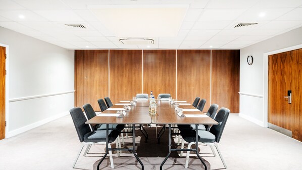 Une salle de conférence avec une longue table, des chaises, une horloge au mur et un lambris en bois.