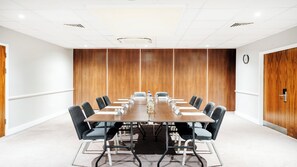 A conference room with a long table, chairs, a clock, and wooden panel walls. - Holiday Inn London - Luton Airport by IHG (Luton)