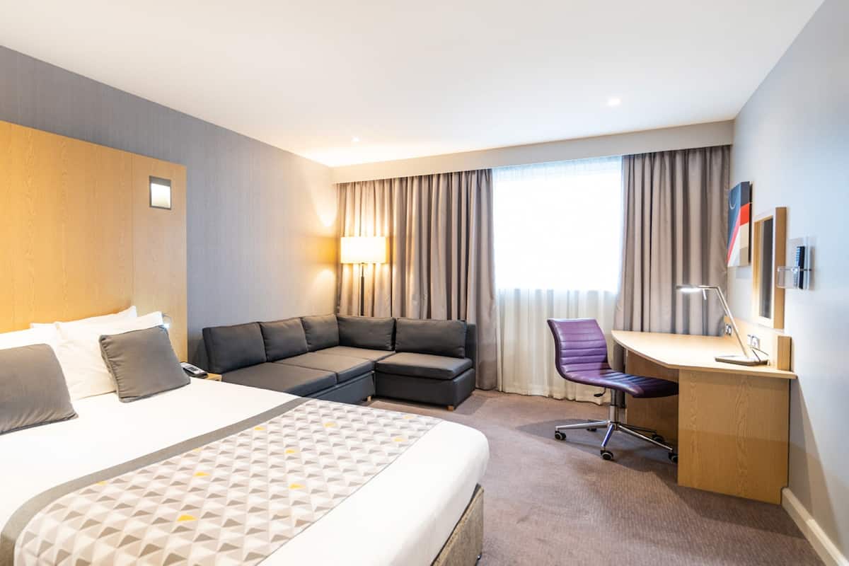 A hotel room with a large bed, a sofa, a desk, and a chair.