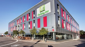 A Holiday Inn hotel with a modern design, featuring a prominent logo, large windows, and outdoor seating. - Holiday Inn London - Luton Airport by IHG (Luton)