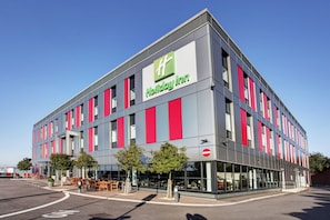 A Holiday Inn hotel with a modern design, featuring a prominent logo, large windows, and outdoor seating.