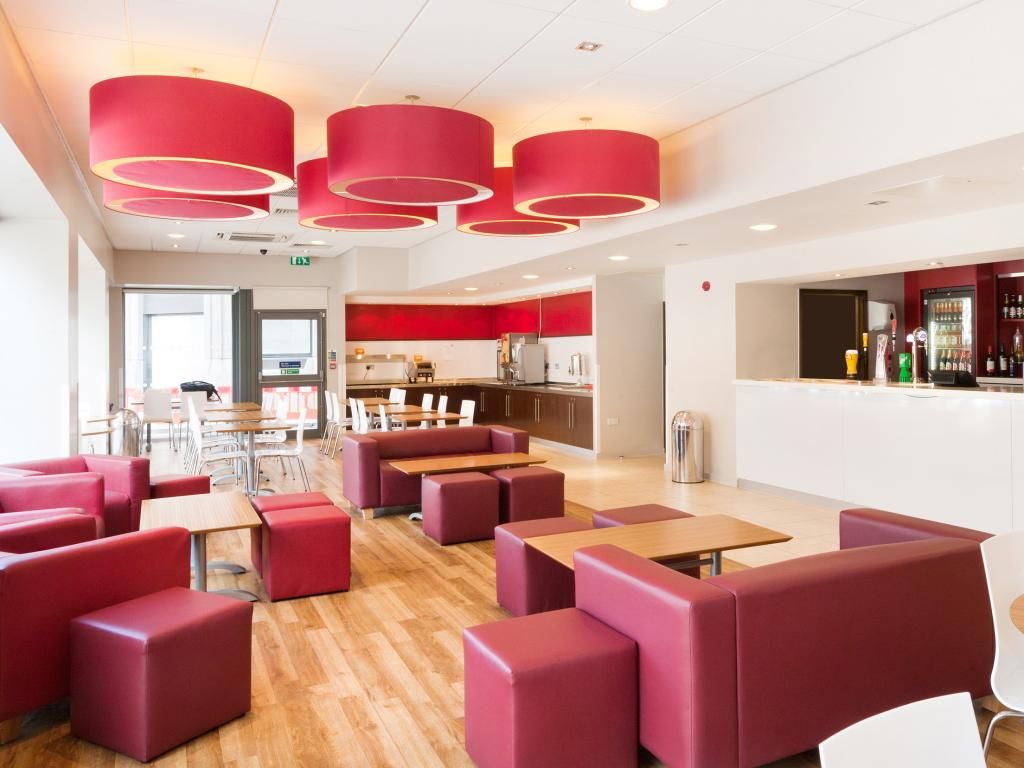 A modern restaurant with red booths and tables, a bar area, and a kitchen visible in the background.