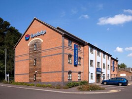 Un hotel Travelodge con fachada de ladrillo, varias ventanas y un estacionamiento con un coche azul.