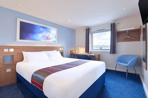 Habitación de hotel con una cama grande, un escritorio, una silla, un televisor y una ventana con cortinas.