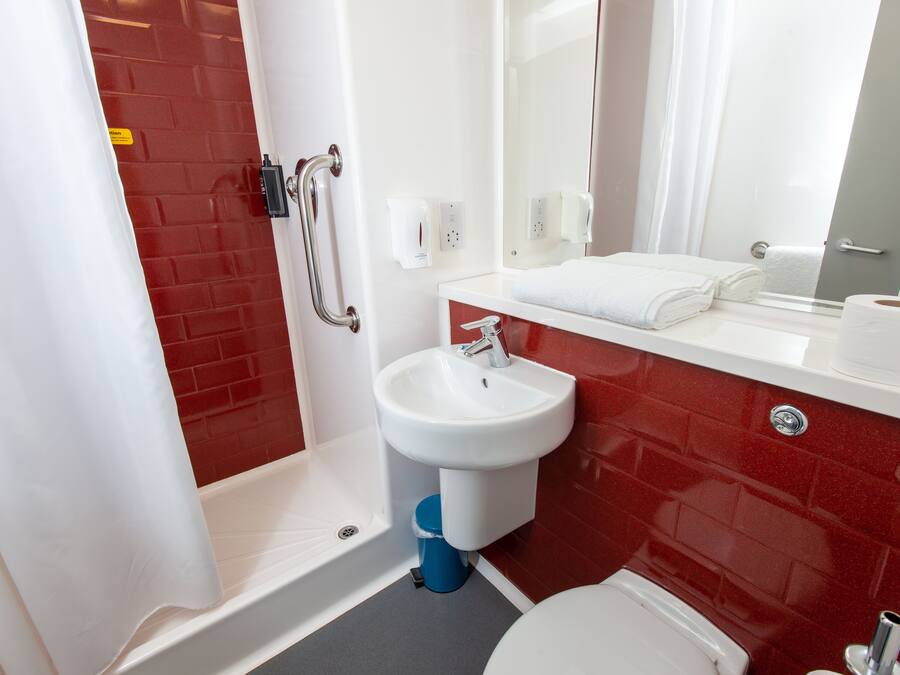 A bathroom with a red-tiled wall, a white sink, a mirror, and a shower area.