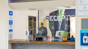A reception desk with a glass partition, a sign indicating COVID-19 safety measures, and a sign for taking care in the hotel. - go2 portishead marina hotel (Bristol)
