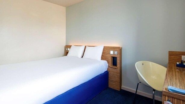 A hotel room with a bed, a chair, and a small table with a lamp. - go2 portishead marina hotel (Bristol)
