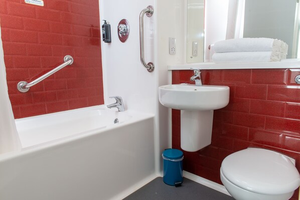 A bathroom with a white bathtub, a white sink, and a white toilet. There are red tiles on the walls and a blue trash can. - go2 portishead marina hotel (Bristol)