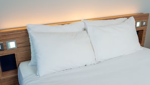 A neatly made bed with white linens and pillows, a wooden headboard with built-in lighting, and a small bedside table with a lamp. - go2 portishead marina hotel (Bristol)