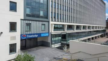 A modern building with a Travelodge sign, large windows, and a covered outdoor area with stairs.