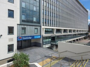 A modern building with a Travelodge sign, large windows, and a covered outdoor area with stairs. - Travelodge London Twickenham (Twickenham)