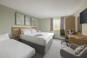 Habitación de hotel con dos camas, un escritorio con silla, televisor y ventana con cortinas.
