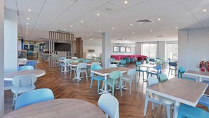A spacious dining area with multiple tables and chairs, a counter with a display, and large windows providing natural light.