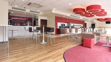 A modern hotel lobby with a bar area, seating arrangements, and a red accent wall.