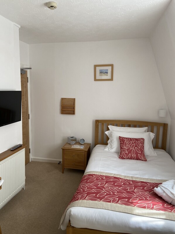 A bedroom with a bed, a nightstand, a framed picture, and a television on a stand. - The Clarence (Weymouth)