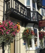 A building with a black iron balcony and hanging flower baskets.