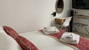 Una habitación de hotel con cama, escritorio, silla, televisor y espejo.