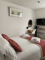 A hotel room with a bed, a desk, a chair, a television, and a mirror.