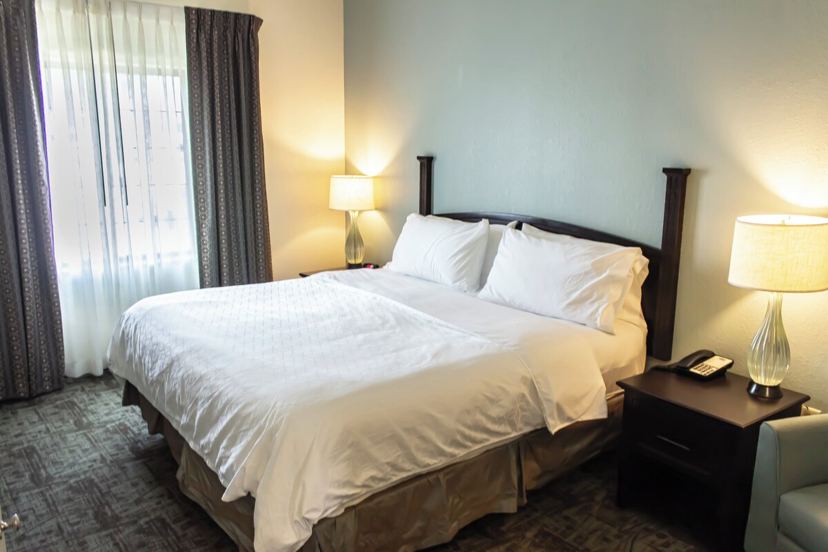 A hotel room with a large bed, a nightstand with a lamp, and a chair.