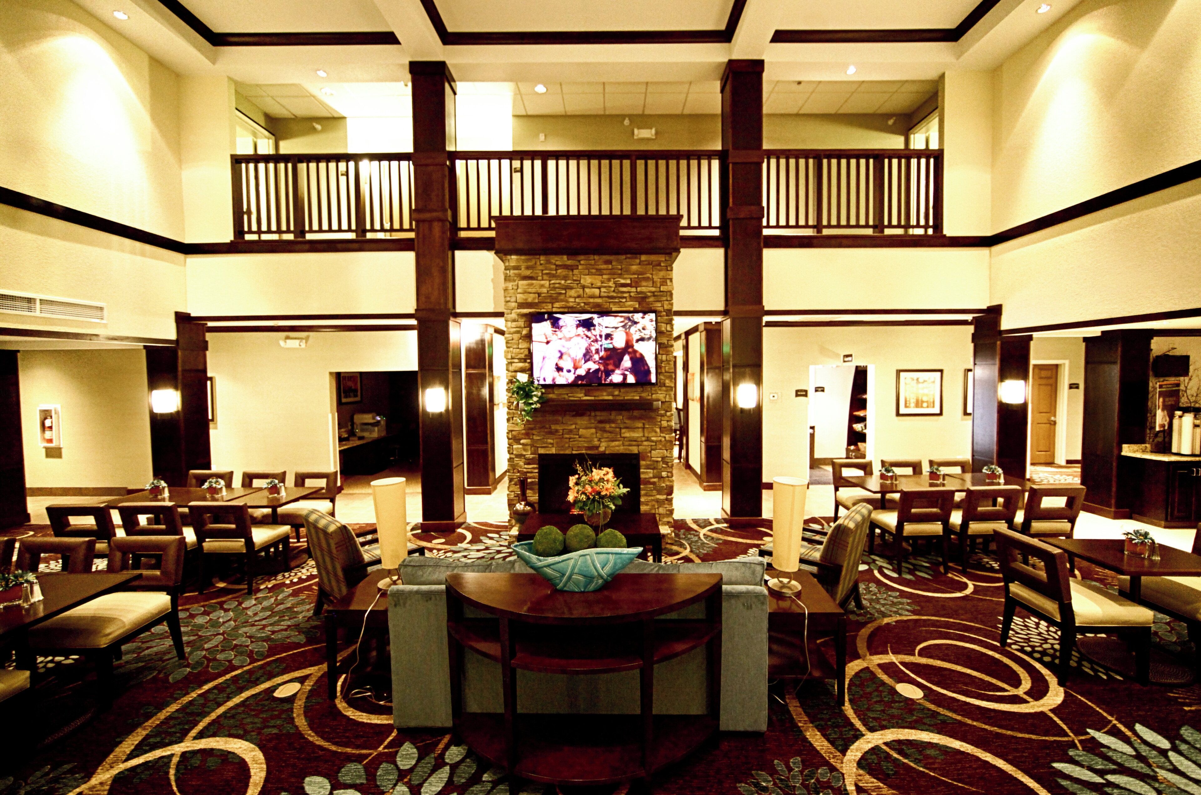 A hotel lobby with a central seating area, a television mounted on a stone wall, and a balcony overlooking the lobby.