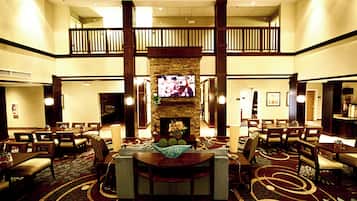 A hotel lobby with a central seating area, a television mounted on a stone wall, and a balcony overlooking the lobby.
