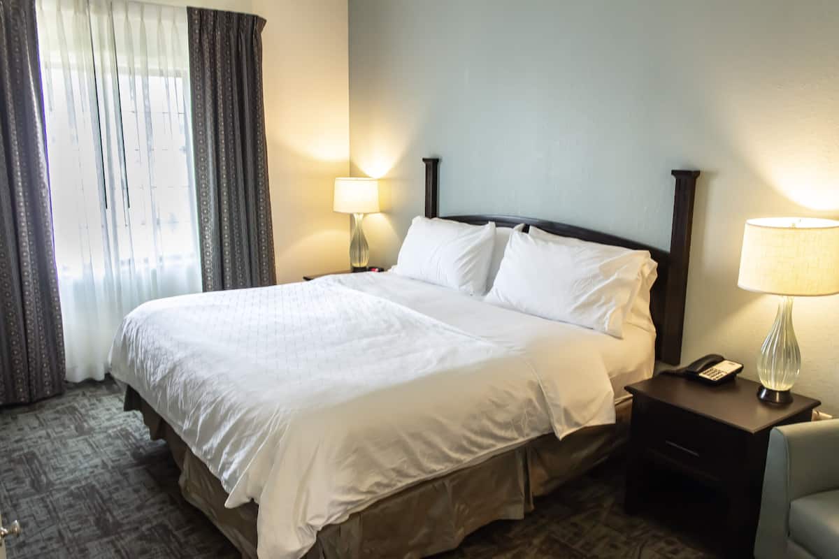 Una habitación de hotel con una cama grande, una mesita de noche con lámpara y una silla.