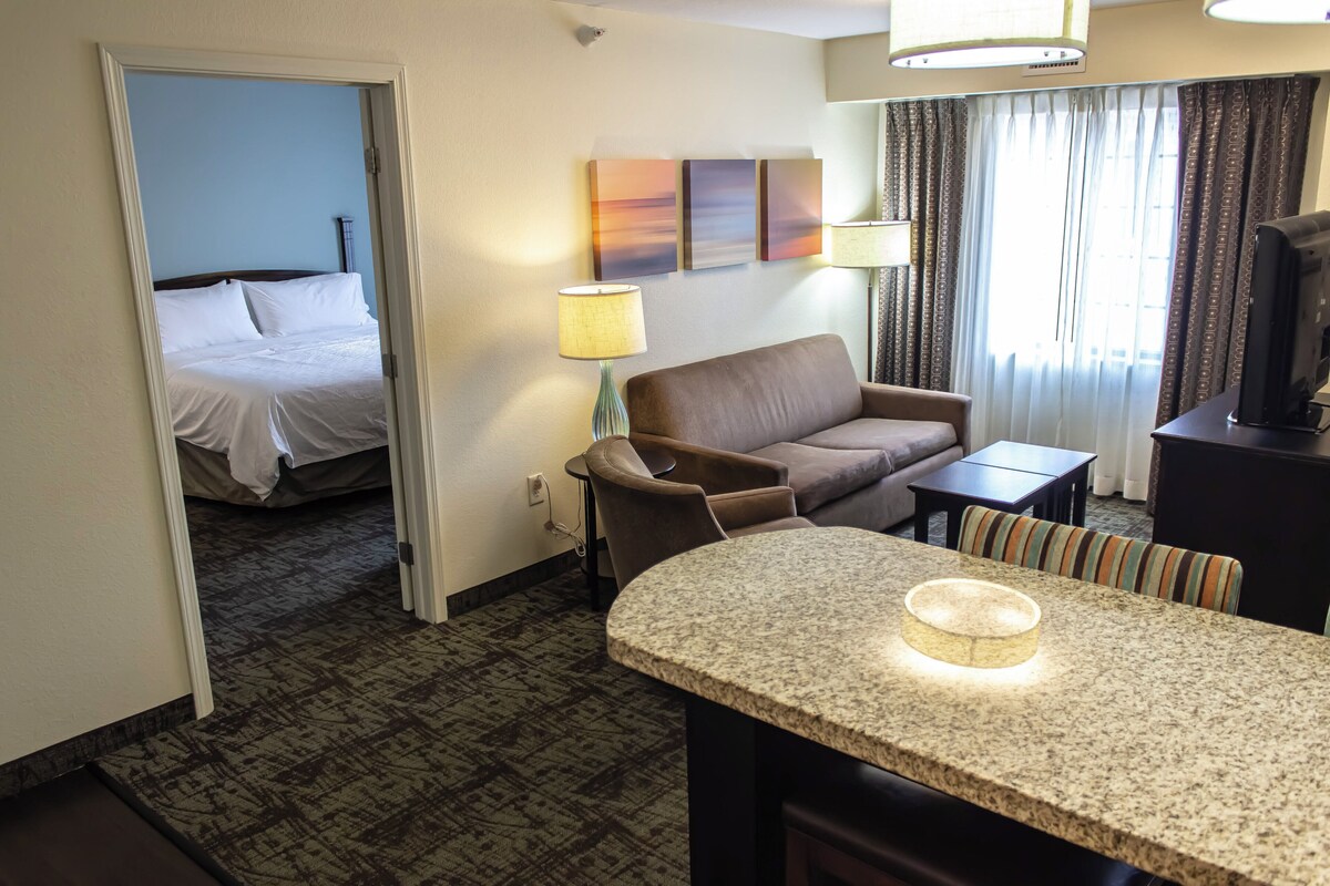A hotel room with a bed, a sofa, a small table, and a television.