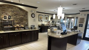 A modern kitchen with granite countertops, dark cabinetry, and a central island. There are various appliances, including a coffee machine and a toaster, and a sign indicating a breakfast buffet.