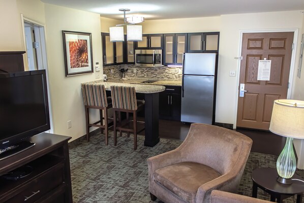 A compact living space with a kitchenette, a flat-screen TV, a striped chair, and a lamp.