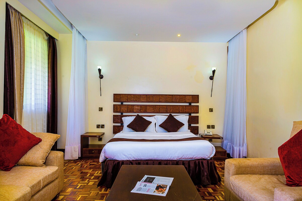 A hotel room with a large bed, two nightstands, a wooden headboard, and two red pillows.