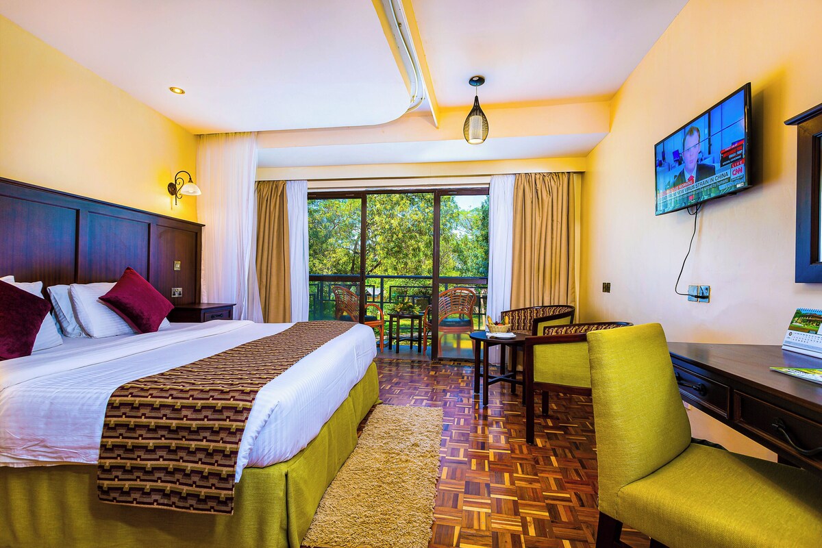 A hotel room with a large bed, a desk with a laptop, a TV, and a view of the outdoors.