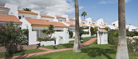 A row of white buildings with red-tiled roofs, surrounded by well-maintained lawns and palm trees.