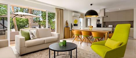 Una sala de estar moderna con un sofá, un sillón verde brillante, una mesa de centro redonda y una zona de comedor con una cocina al fondo.