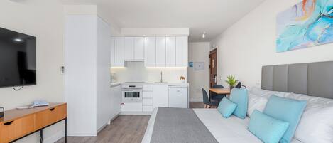 A modern hotel room with a large bed, a desk, a TV, and a kitchenette.
