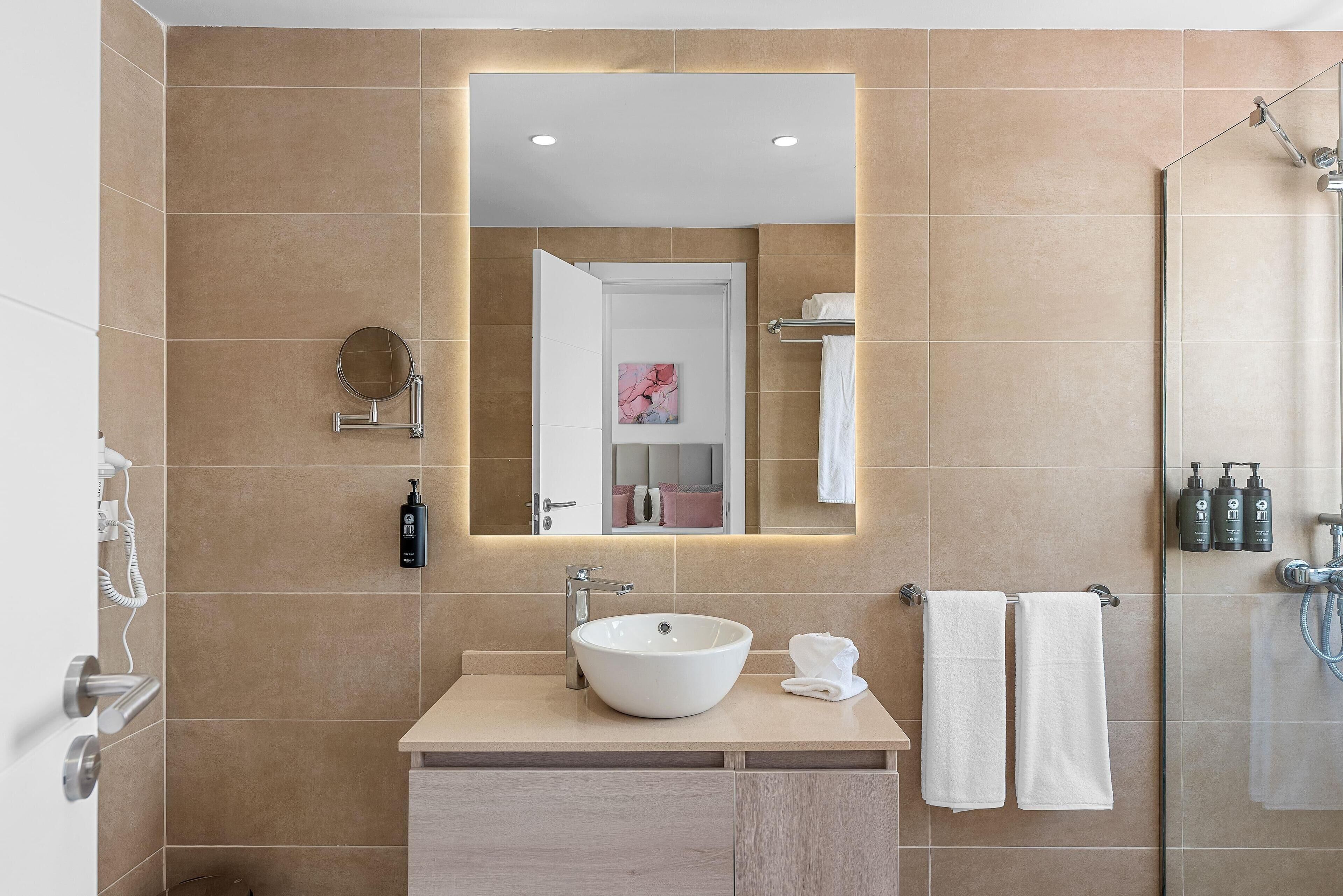 A modern bathroom with a large mirror, a sink, and a shower.