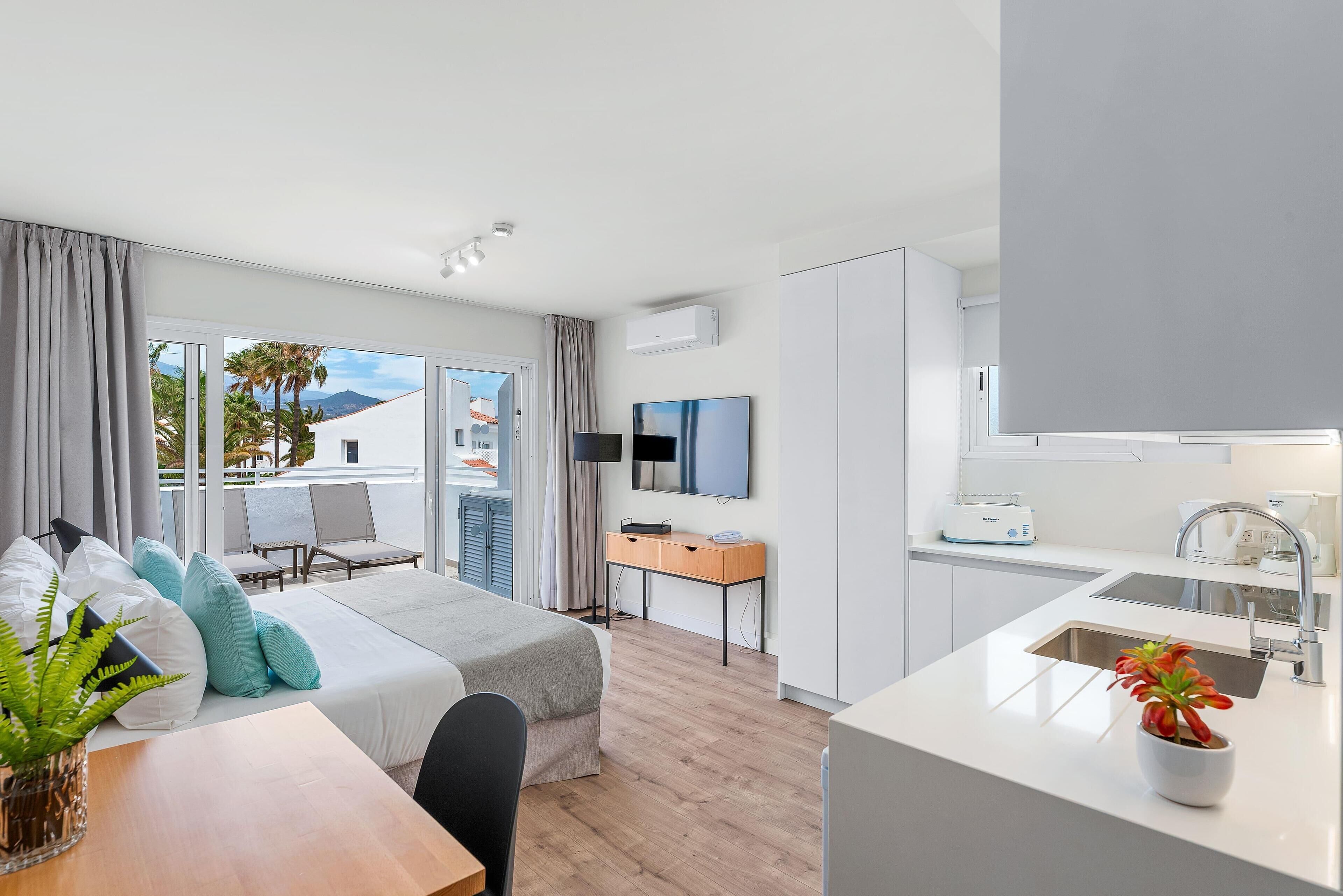 Una habitación de hotel moderna con balcón, zona de comedor y kitchenette.