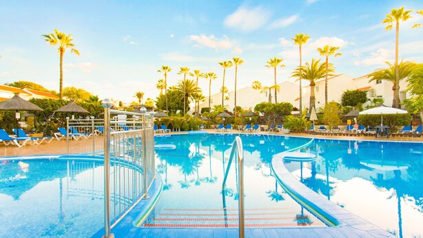 A swimming pool with blue water, surrounded by palm trees and lounge chairs. - Wyndham Residences Golf del Sur (San Miguel de Abona)