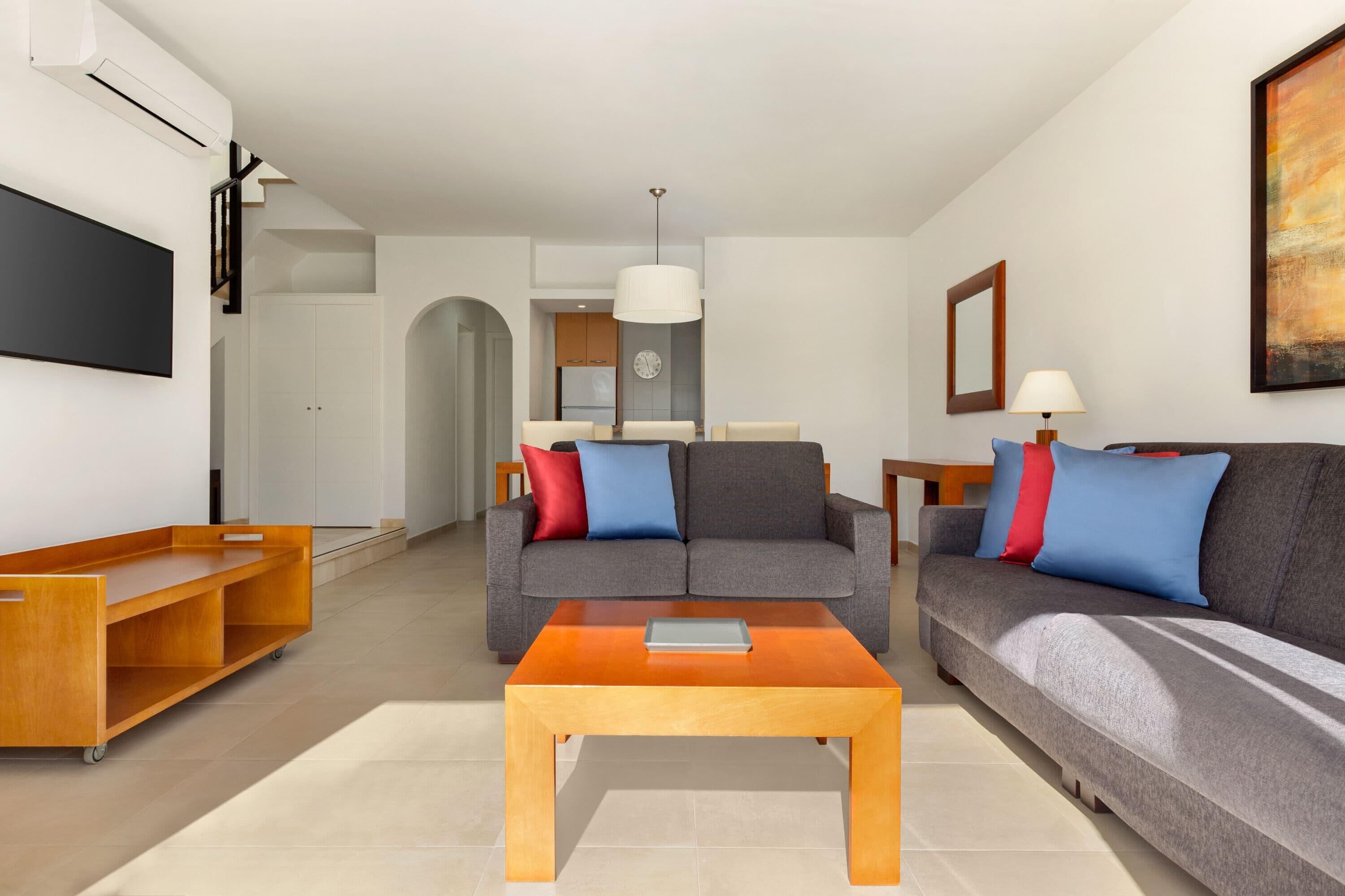 A modern living room with a grey sofa, wooden coffee table, and a TV on the wall.