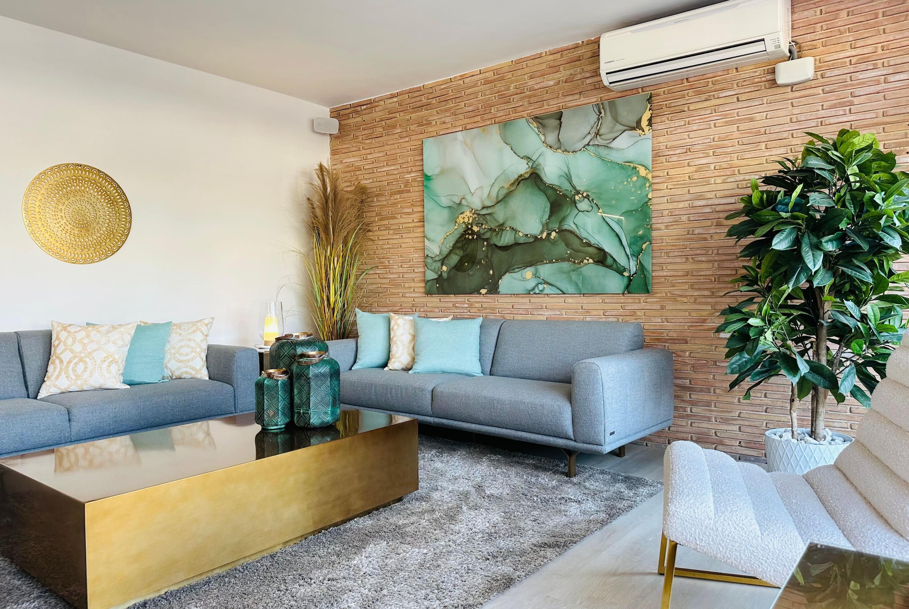 A modern living room with a grey sofa, a coffee table, and a large abstract painting on the brick wall.