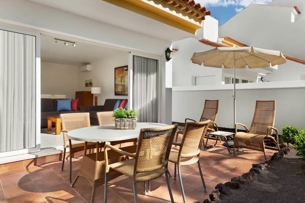 An outdoor patio with a round table, wicker chairs, and a large umbrella.