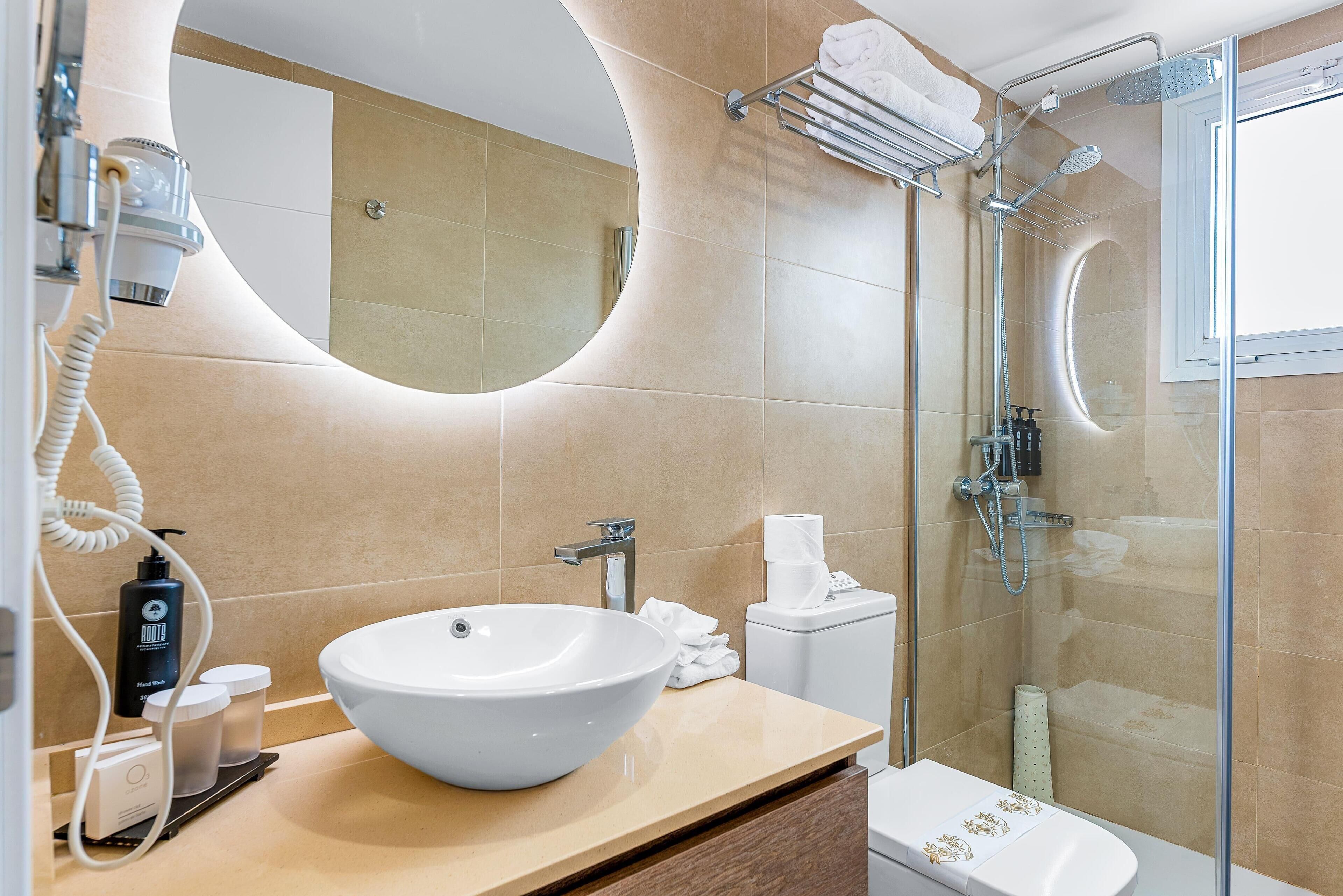 A modern bathroom with a large oval sink, a glass-enclosed shower, and a toilet with a paper towel dispenser.