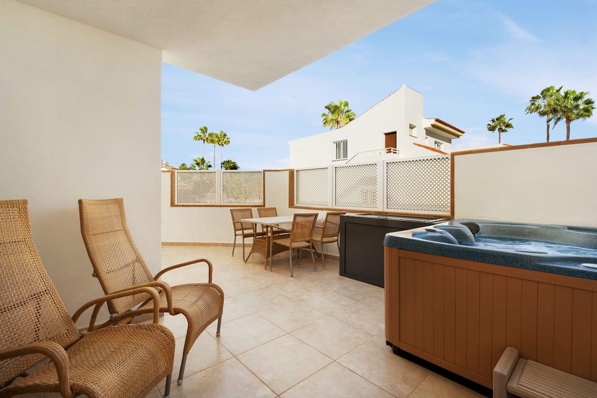 A patio with wicker chairs, a table, and a hot tub.