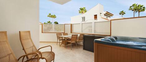 A patio with wicker chairs, a table, and a hot tub.