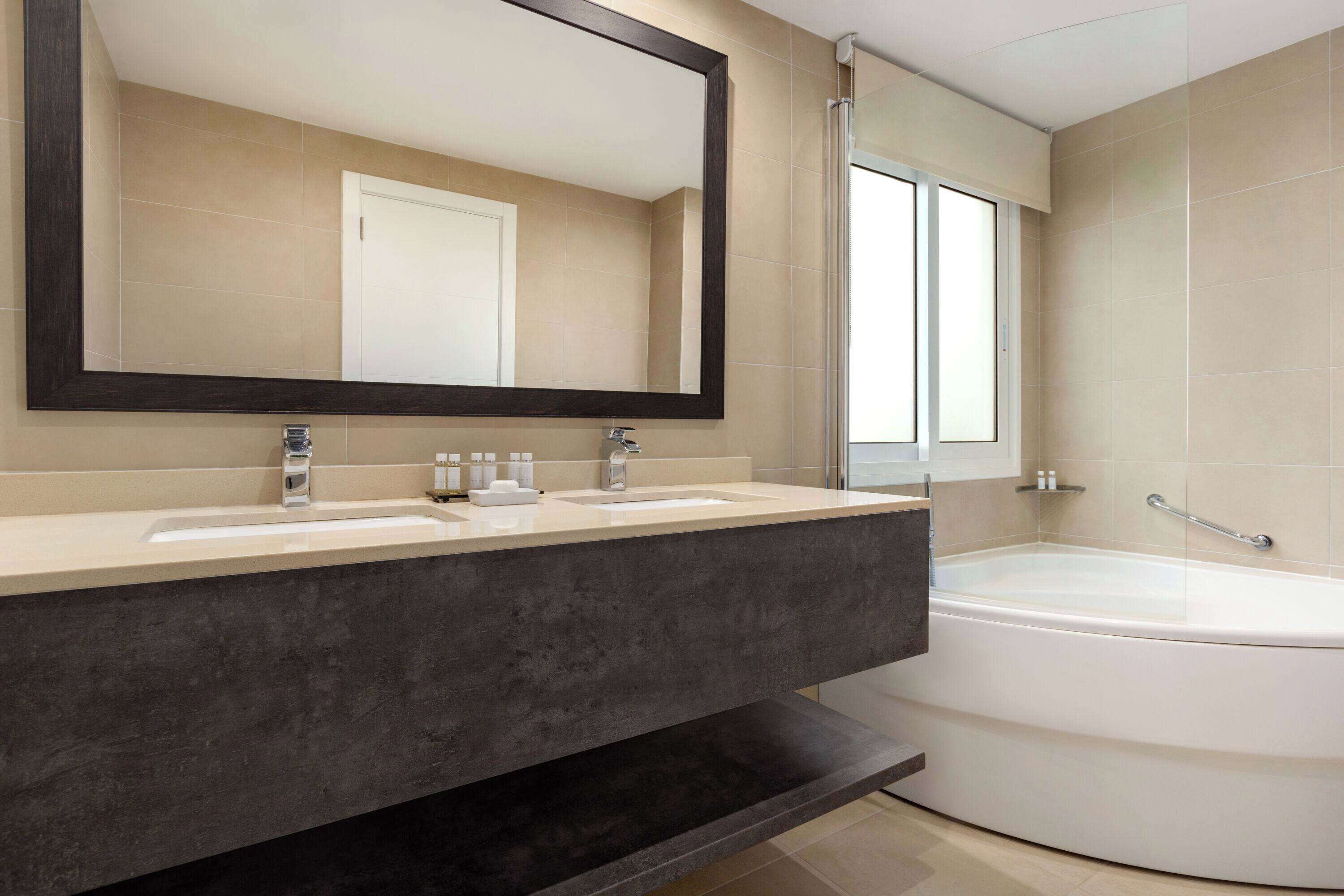 A modern bathroom with a large mirror, two sinks, a bathtub, and a shower.