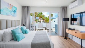 A modern hotel room with a large bed, a desk, a TV, and a balcony with a view of palm trees and buildings. - Wyndham Residences Golf del Sur (San Miguel de Abona)