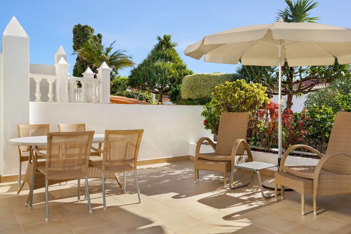 An outdoor patio with wicker furniture, a white table, and a large umbrella.