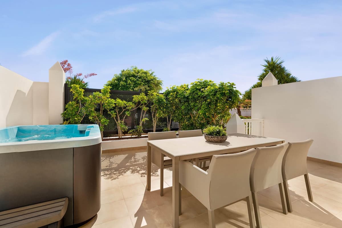 A rooftop terrace with a hot tub, a table with chairs, and potted plants.
