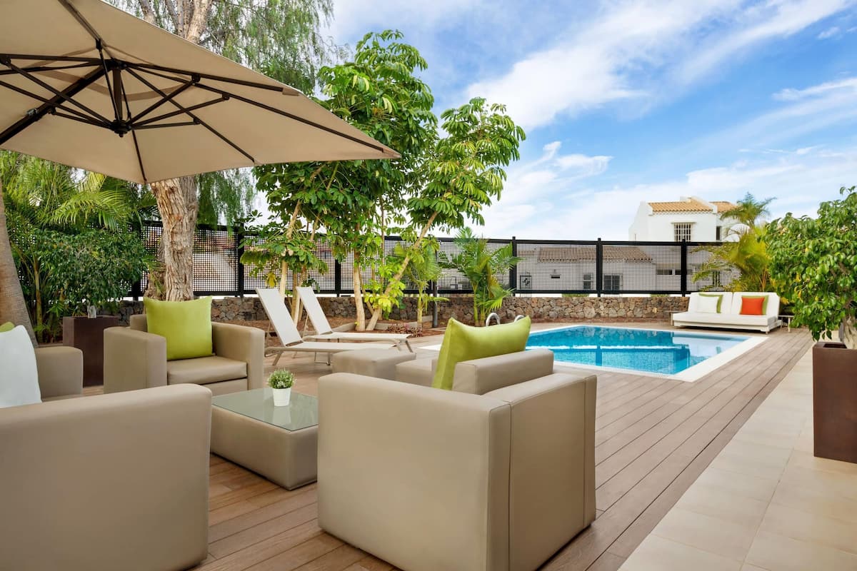 A poolside area with beige sofas, a glass table, and a large umbrella.
