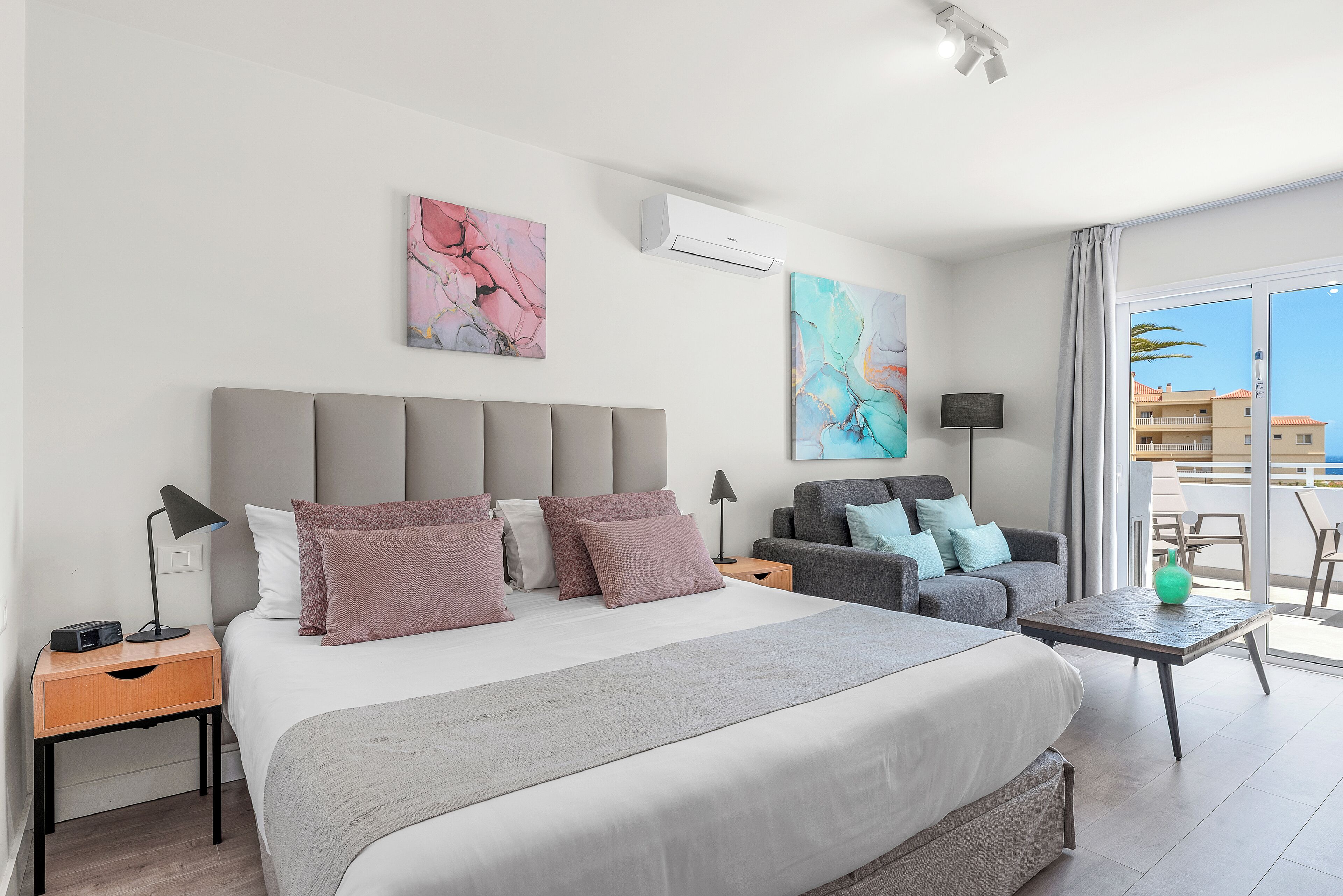 Una habitación de hotel moderna con una cama grande, un sofá, una mesita y obras de arte en las paredes.