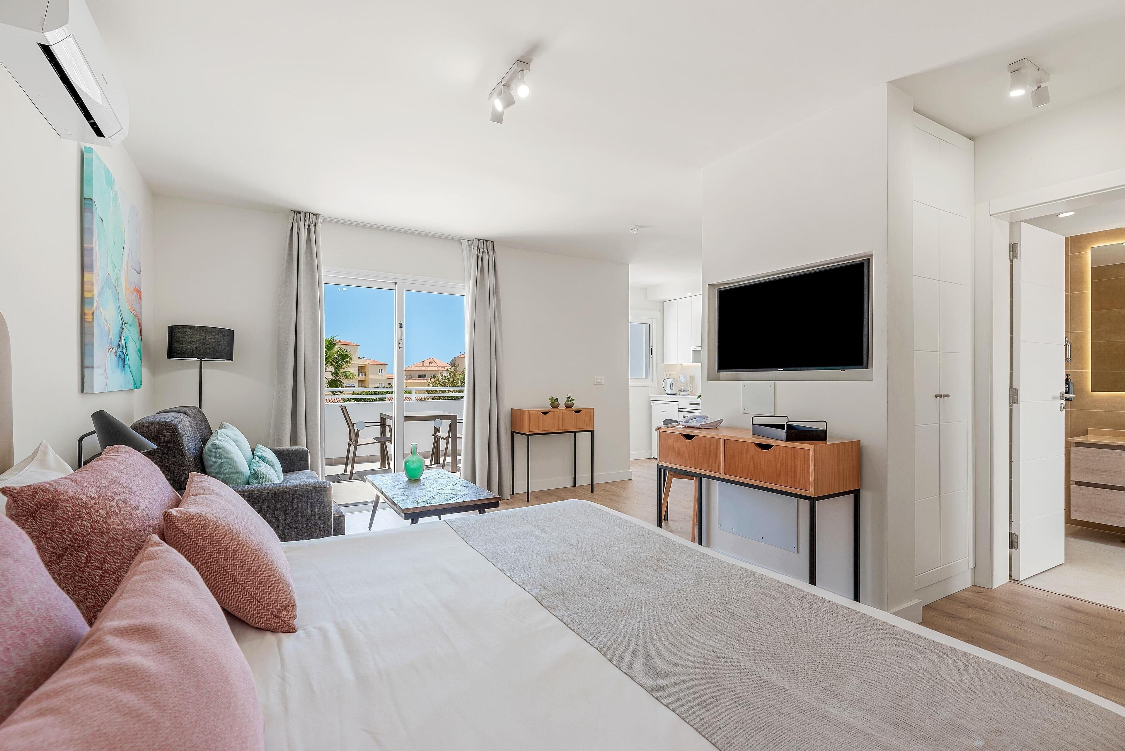 Een moderne hotelkamer met een groot bed, een bureau, een flatscreen-tv en een balkon met uitzicht.
